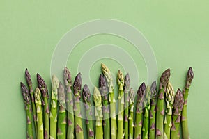 Heap of fresh asparagus on green background top view. Healthy food in flat lay style