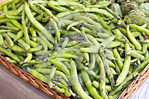 Heap of fresh green pods of broad beans in wicker tray