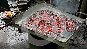 Heap of glowing heated charcoals being added on the tray over a brazier during baking Portuguese-Siamese Kudeejeen cupcakes