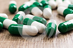 Heap of green and white capsules on wooden background.