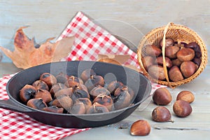 Heap of grilled edible chestnuts in cast iron skillet with textile napkin