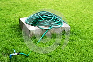 Heap of hose on concrete stand and faucet with grass field background