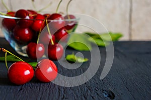 A heap and a large glass bowl of fresh red ripe cherries and green leaves of a cherry