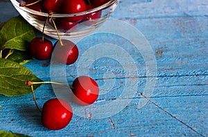 A heap and a large glass bowl of fresh red ripe cherries and green leaves of a cherry tree