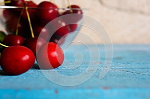 A heap and a large glass bowl of fresh red ripe cherries and green leaves of a cherry tree