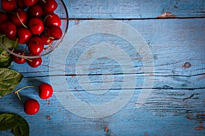 A heap and a large glass bowl of fresh red ripe cherries and green leaves of a cherry tree