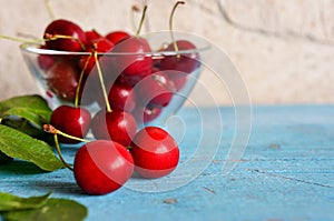 A heap and a large glass bowl of fresh red ripe cherries and green leaves of a cherry tree