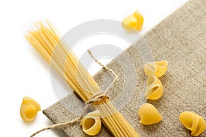 Heap of macaroni shells and spaghetti with rope on brown bagging