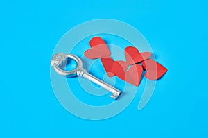 Heap of many red paper hearts near silver vintage key lies on blue countertop. Concept of closed or opened love or Valentines day