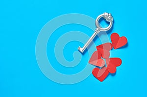 Heap of many red paper hearts near silver vintage key lies on blue countertop. Concept of closed or opened love or Valentines day