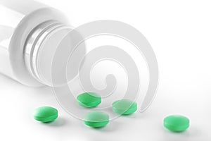 Heap of medical pills in green colors and plastic white bottle. Pills on white background. Concept of healthcare and medicine.