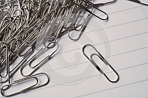 Heap of metal paper clips on white lined paper notepad as a symbol of typical office environment