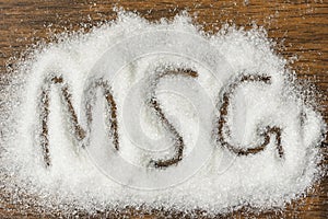 Heap of monosodium glutamate on wooden background with text MSG