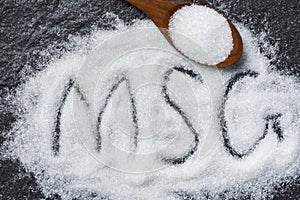 Heap of monosodium glutamate on wooden spoon and dark background - text MSG