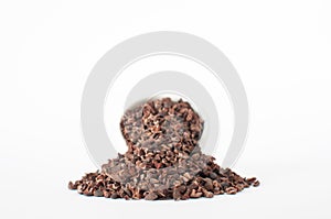Heap of organic raw cacao nibs, with full of white ceramic bowl on back.
