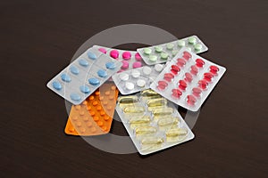 Heap of packs of pills and capsules isolated on brown wooden background