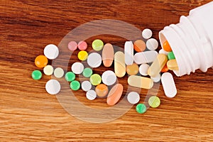 Heap of pills near the opened container on wooden desk