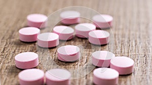 Heap of pink capsules on wooden background.