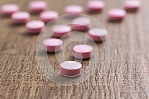 Heap of pink capsules on wooden background. Pills are shaping a