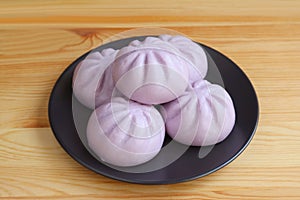 Heap of purple sweet potato steamed buns on black plate served on wooden table