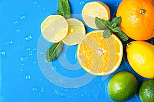 Heap of raw juicy citrus fruits oranges lemons lime fresh mint on wet blue background with water drops. Summer beverages