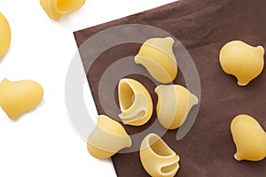 Heap of raw macaroni shells on brown napkin, selective focus.