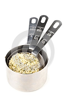 Heap of raw, organic hemp seeds in metal measurement scoop over white