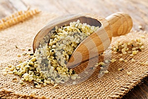 Heap of raw, organic hemp seeds in wooden scoop on burlap on rustic table