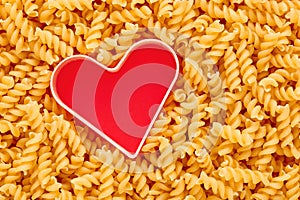 Heap of raw rotini or fusulli pasta with a red heart shape with copy space