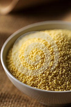 Heap of raw, uncooked couscous in white bowl on burlap