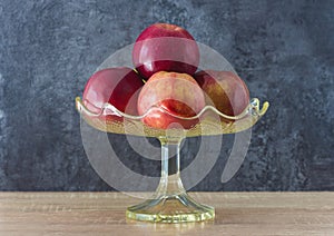 Heap of red apples in a vintage glass vase on a wooden table