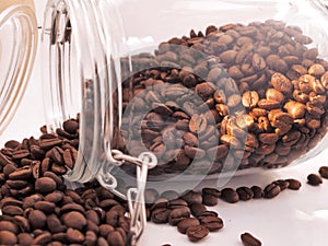 Heap of roasted coffee beans from jar around white background