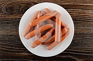 Heap of sausages in shell in plate on wooden table. Top view