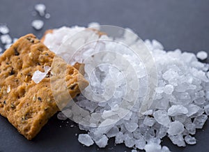 Heap of sea salt and salty crackers. Black surface.