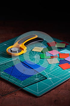 Heap square pieces of colorful fabrics, rotary cutter and ruler on cutting mat