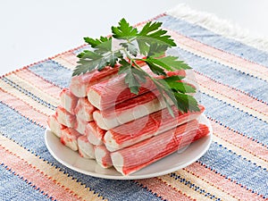 Heap of surimi crab sticks and parsley on a white saucer over a striped table mat. Seafood and ingredient for salads. Healthy