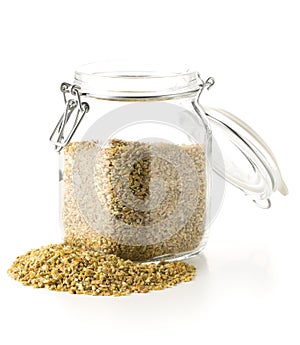 Heap of uncooked, raw freekeh or firik, roasted wheat grain, in glass storage jar over white photo