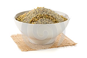 Heap of uncooked, raw freekeh or firik, roasted wheat grain, in white bowl over white photo