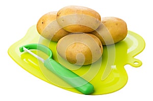 Heap of washed potatoes and peeler on plastic cutting board isolated on white