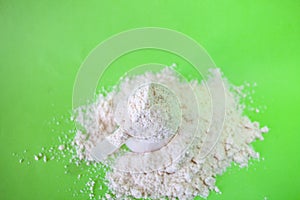 Heap of whey protein powder with plastic spoon on green background