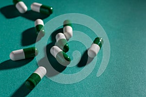 Heap of white and green capsules on green background.