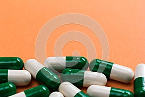 Heap of White and green capsules on orange background.