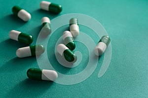 Heap of white and green capsules on green background.