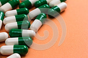 Heap of White and green capsules on orange background.