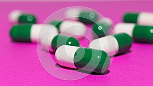 Heap of white and green capsules on purple background.