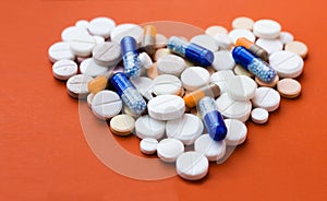 Heap of white pills, tablets in shape of heart, capsules on red orange background. Drug prescription for treatment medication