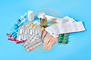 Heap of white pills and yellow capsules, bottle, syringes, bandage, patches and ampoules with red vaccine on blue background