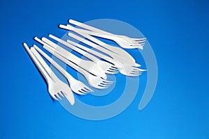 White plastic knives and forks. Disposable plastic tableware on blue background
