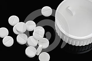 Heap of white tablets medicine lying beside of plastic bottle. Pills and bottles are white. Isolated on black