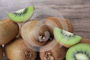 Heap of whole and cut fresh kiwis near wooden wall, closeup